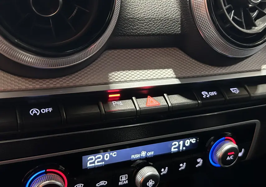 Gros plan sur la console centrale de l’Audi Q2 gris, montrant les commandes de climatisation et les voyants lumineux.