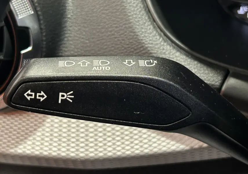 Gros plan sur la manette de clignotants noire avec pictogrammes blancs dans l’Audi Q2 gris 2023 TFSI.