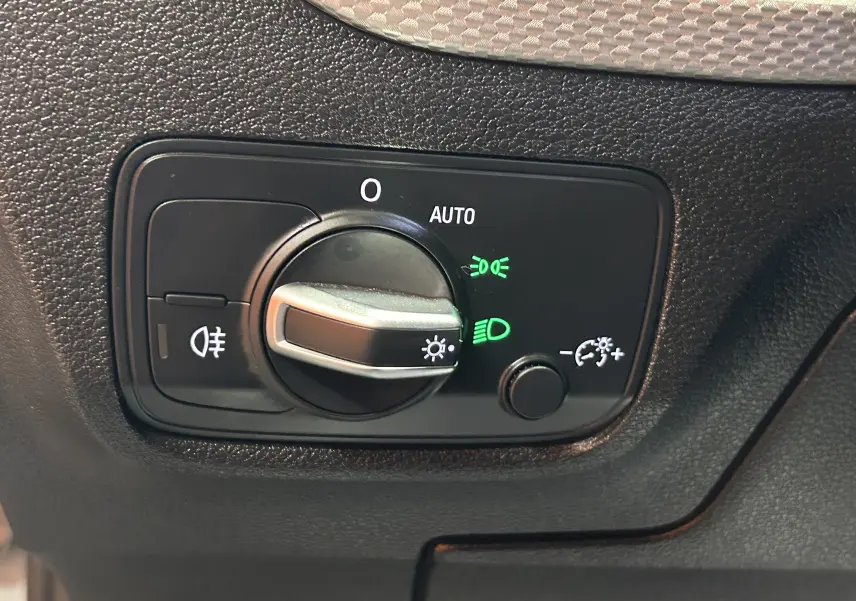 Gros plan sur le bouton de commande des phares avec indicateurs verts, sur le tableau de bord noir de l'Audi Q2 2023.