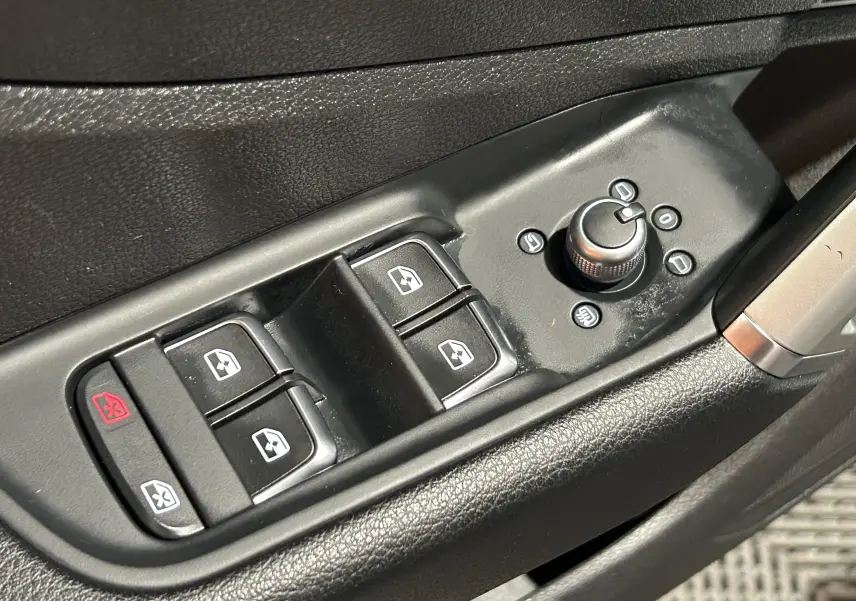 Gros plan sur les commandes de lève-vitres et réglage des rétroviseurs côté conducteur d’un Audi Q2 gris, intérieur noir.