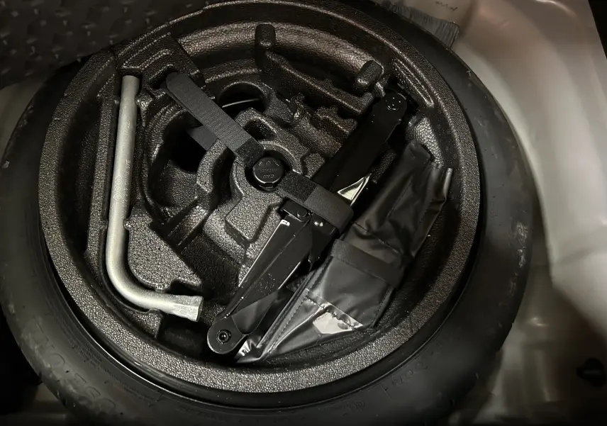 Roue de secours avec outils de changement rangés dans le coffre d’un Audi Q2 gris, vue en plongée.