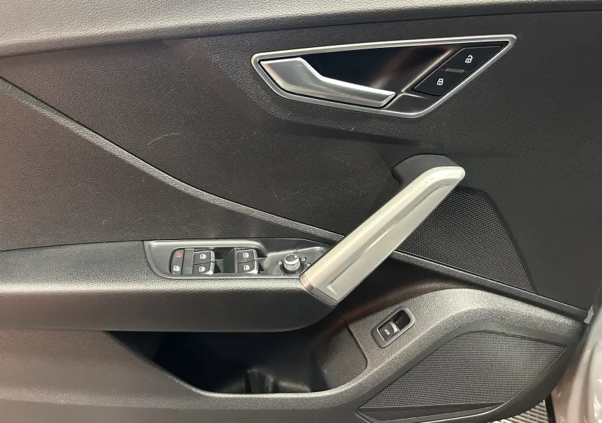Vue rapprochée de la porte intérieure côté conducteur de l'Audi Q2 gris avec commandes de vitres et poignée argentée.