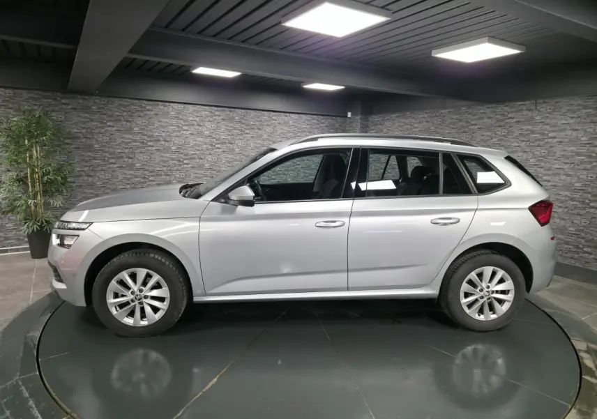Vue de profil côté gauche d’un Skoda Kamiq gris métallisé 2023 en intérieur avec jantes alliage 16 pouces.