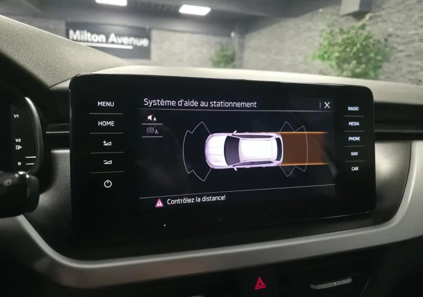 Écran tactile intérieur du Skoda Kamiq 2023 montrant l'aide au stationnement avec vue du véhicule en blanc.
