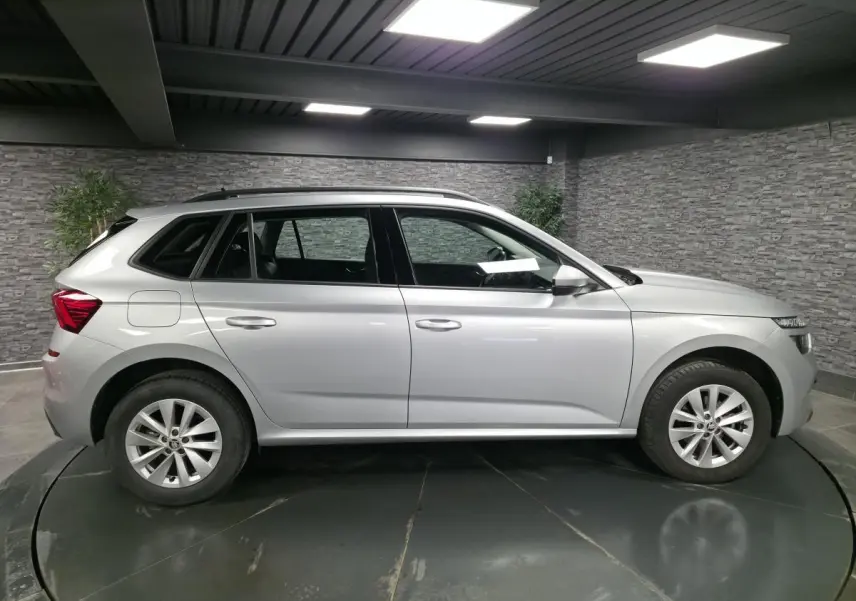 Vue de profil côté gauche d'un Skoda Kamiq gris métallisé 2023, avec jantes alliage et barres de toit noires.
