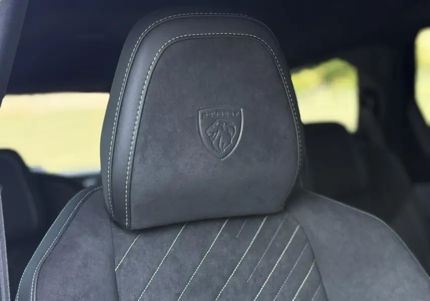 Gros plan sur l’appui-tête en Alcantara noir avec logo Peugeot embossé, intérieur du Peugeot 5008 Hybrid GT 2026.