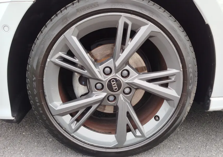 Gros plan sur la roue avant droite d’une Audi A3 Sportback blanche avec jante alliage S line grise et logo Audi central.