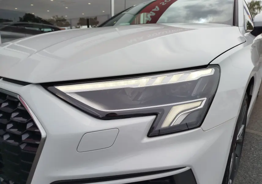 Gros plan sur le phare avant droit blanc glacier métallisé de l'Audi A3 Sportback 30 TFSI S line 2022.