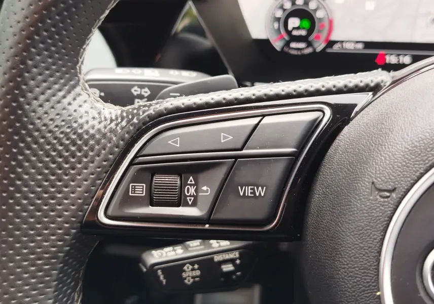 Gros plan sur les commandes multifonctions à gauche du volant perforé noir de l’Audi A3 Sportback blanc Glacier.