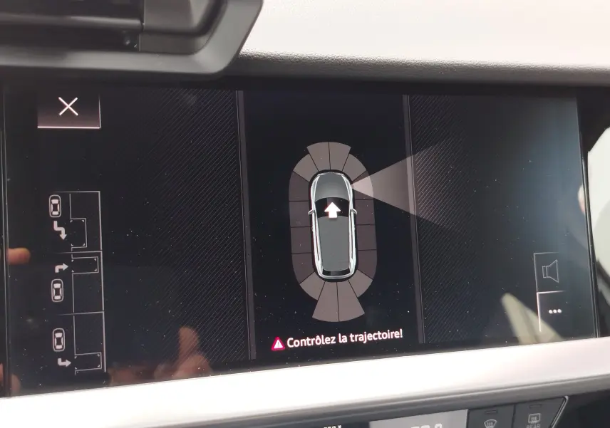 Écran intérieur affichant l’aide au stationnement de l’Audi A3 Sportback blanc glacier, vue de dessus virtuelle du véhicule.