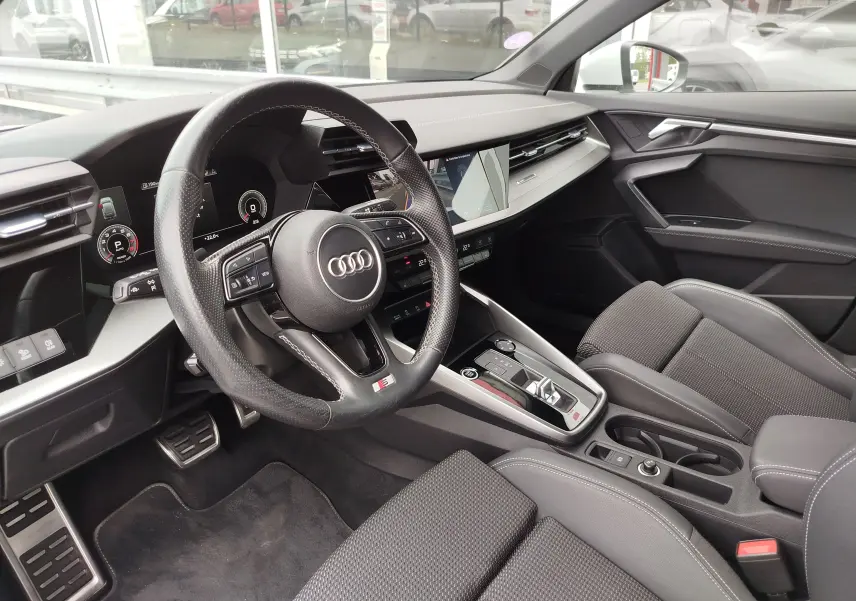 Vue intérieure côté conducteur de l'Audi A3 Sportback 30 TFSI S line 2022 avec volant sport et sellerie tissu gris.