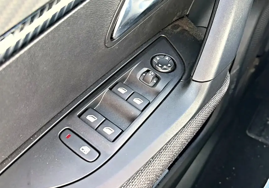 Gros plan sur les commandes de vitres électriques côté gauche d'une Peugeot 2008 gris, avec bouton de verrouillage activé.