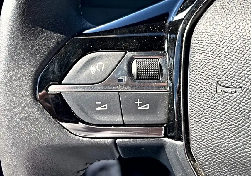 Gros plan sur les commandes de volume et appel mains-libres sur le volant noir du Peugeot 2008 gris.
