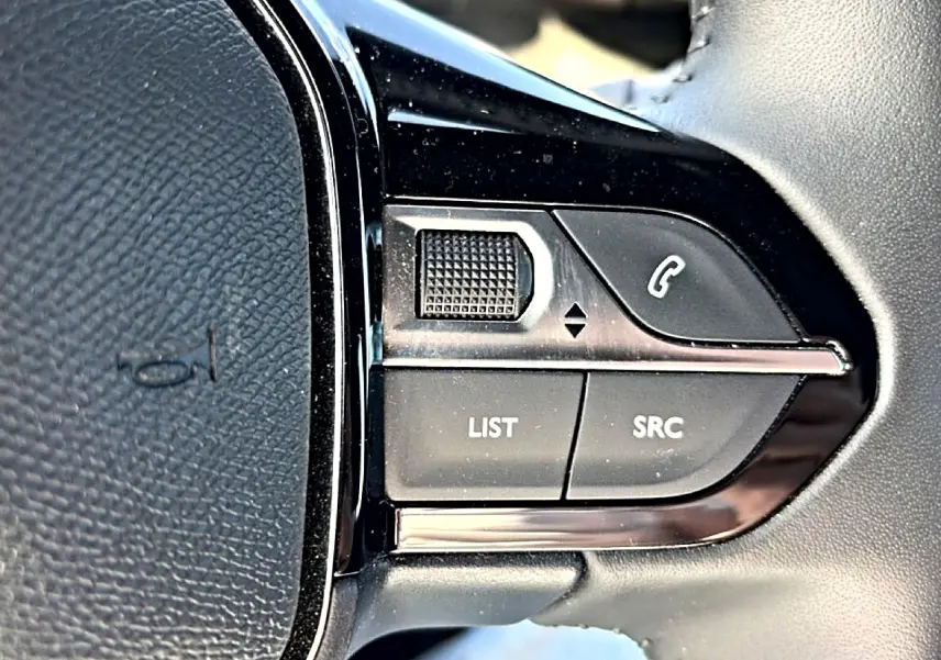 Gros plan sur les commandes gauche du volant noir du Peugeot 2008 gris, avec boutons multifonctions et molette.