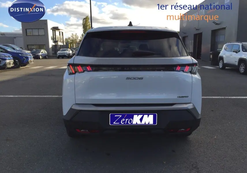 Vue arrière d'un Peugeot 5008 blanc Okenite Metal avec feux LED distinctifs et badge Hybrid sur un parking.