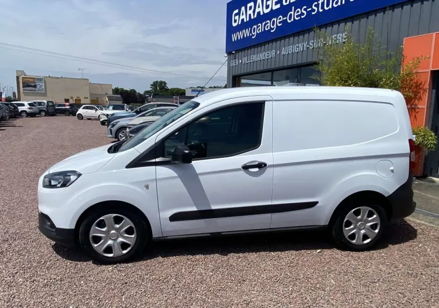 Fourgon Ford Tourneo Courier blanc vu de profil côté gauche, avec porte latérale coulissante et enjoliveurs cache moyeu.