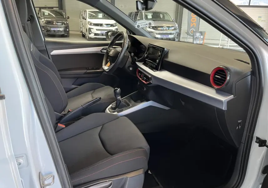 Intérieur côté conducteur du SEAT Arona blanc Nevada 2024, avec tableau de bord noir et aérateurs rouges.