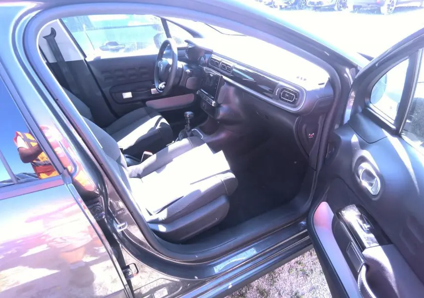 Intérieur avant droit d'une Citroën C3 gris foncé 2024, montrant sièges tissu et tableau de bord noir brillant.