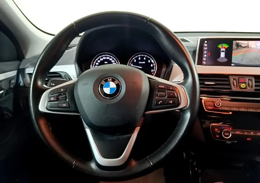 Vue rapprochée du volant cuir et alu noir de la BMW X2 sDrive18i 2023 avec tableau de bord et écran multimédia allumé.