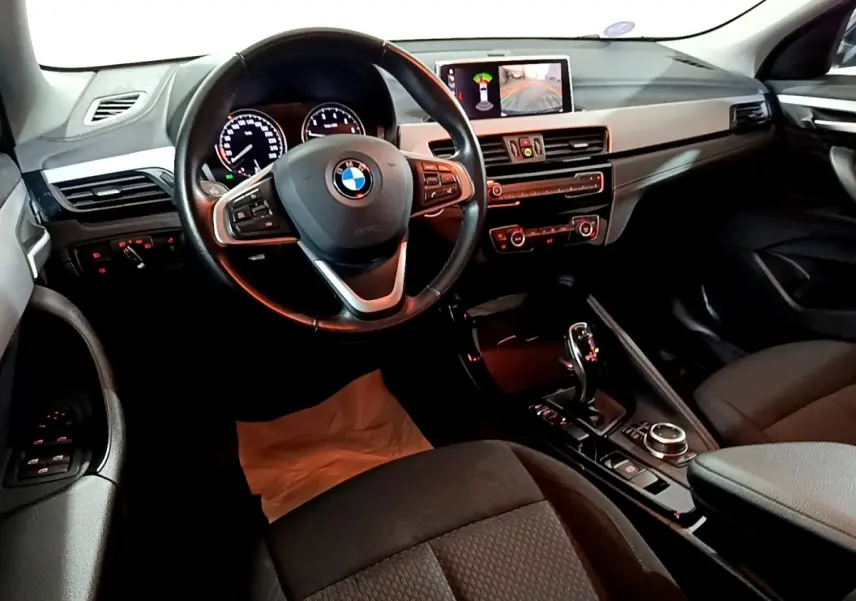 Vue intérieure côté conducteur du BMW X2 sDrive18i 2023, volant cuir alu multifonctions et écran central affichant caméra de recul.