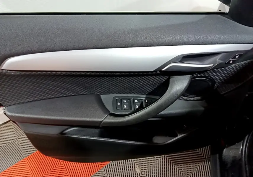 Gros plan sur la porte côté conducteur de la BMW X2 noire, mettant en valeur la poignée, les commandes de vitres et la finition alu.
