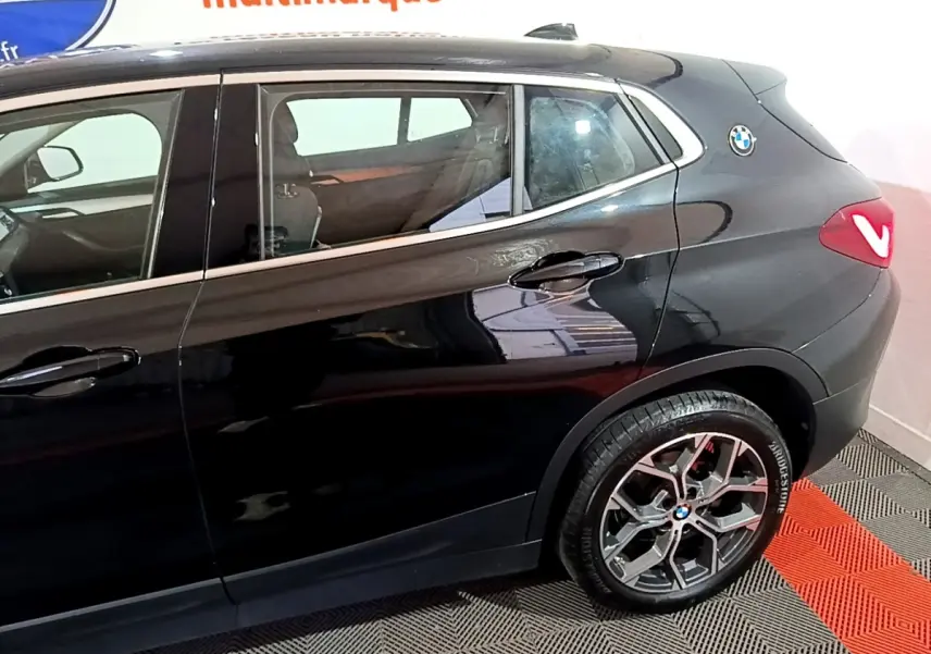 Vue latérale droite sur la partie arrière d’un BMW X2 noir 2023 avec jante alliage et logo BMW sur l’aile arrière.