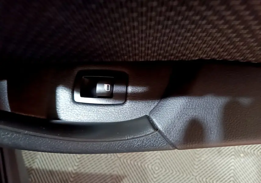 Gros plan sur la poignée intérieure noire et l’interrupteur de lève-vitre côté conducteur du BMW X2 noir 2023.