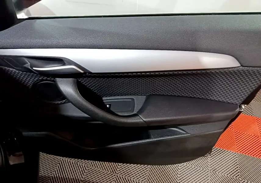 Gros plan sur la porte côté gauche de la BMW X2 sDrive18i Lounge 2023, avec garniture noire et insert argenté.