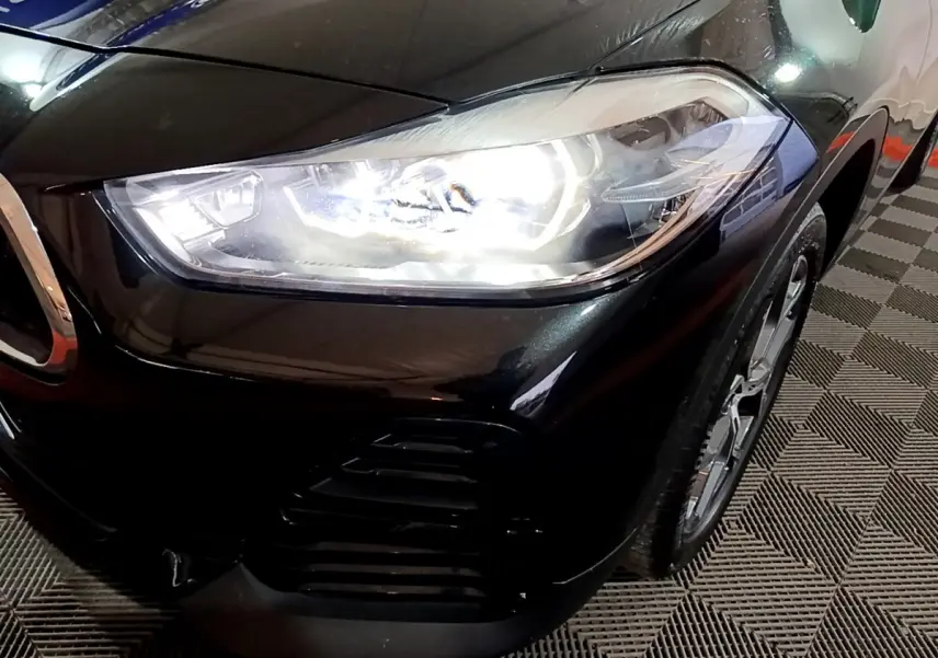 Gros plan sur l'avant droit noir brillant du BMW X2 sDrive18i 2023 avec phare LED allumé et jante visible.