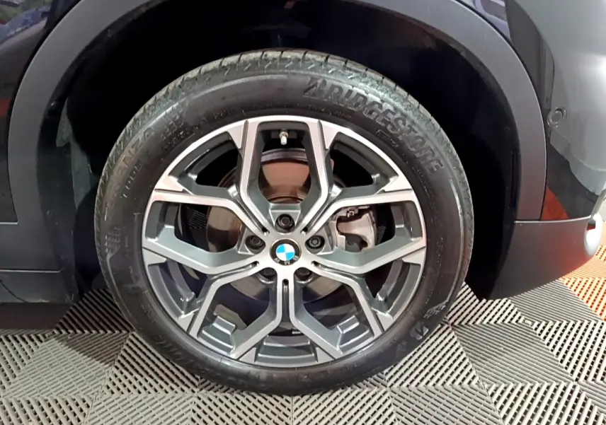 Gros plan sur la roue avant gauche noire d’un BMW X2 2023 avec jante alliage à design moderne.