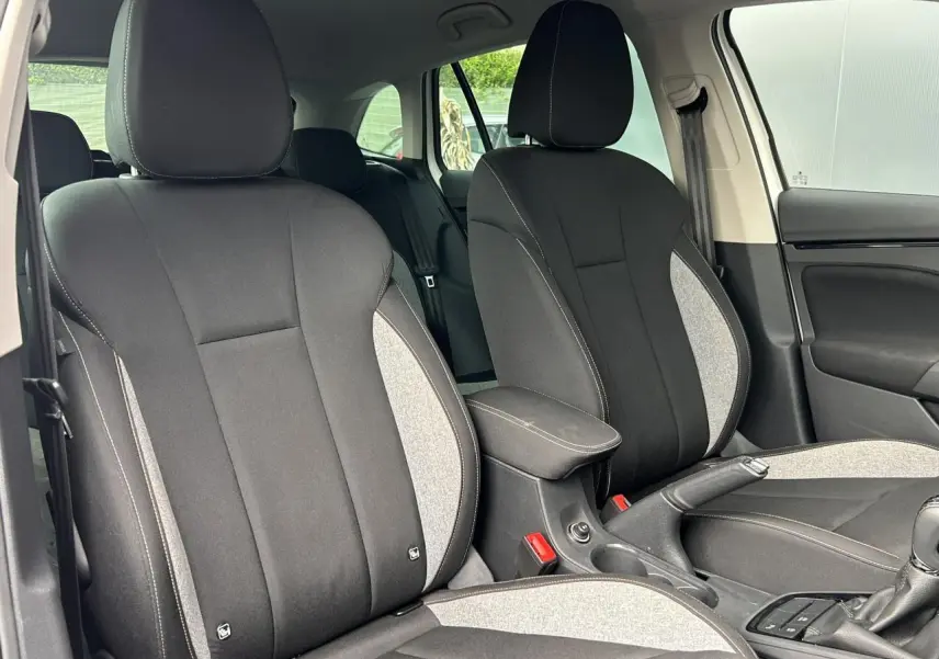 Vue intérieure des sièges avant en tissu noir et gris de la Skoda Scala TSI 116 DSG7 Sélection, avec accoudoir central.