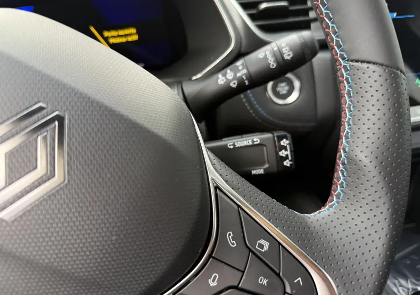 Gros plan sur le volant en cuir perforé avec surpiqûres tricolores du Renault Symbioz Esprit Alpine 2026, boutons multifonctions visibles.