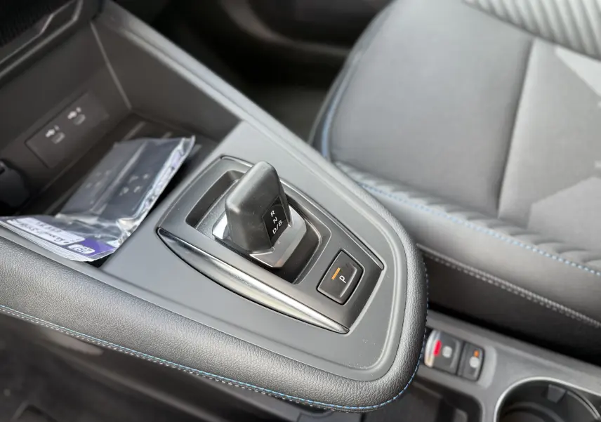 Gros plan sur le levier de vitesses automatique et le bouton parking, avec surpiqûres bleues sur la console intérieure grise.