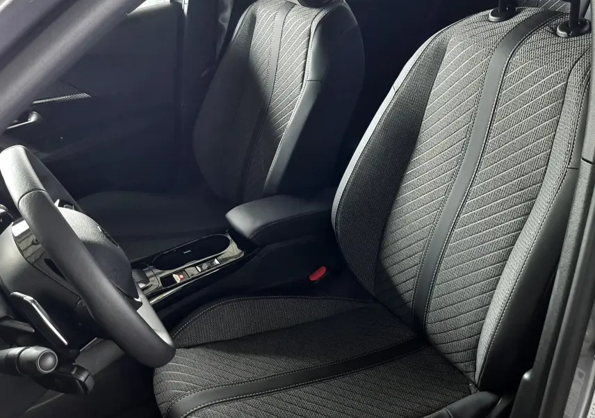 Vue intérieure côté conducteur du Peugeot 2008 gris Artense 2025, sièges tissu noir avec surpiqûres et accoudoir central.