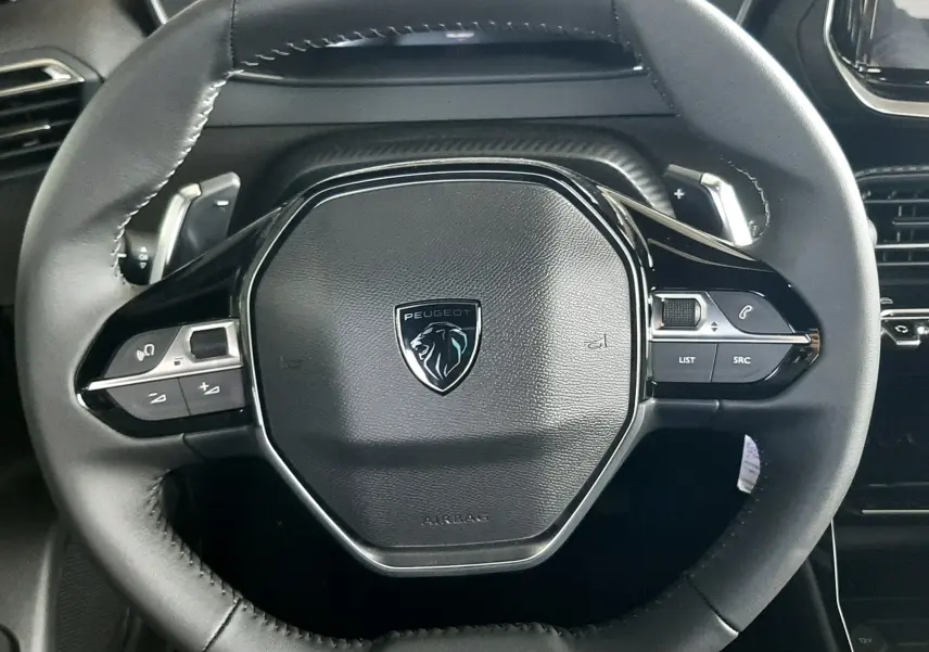 Gros plan sur le volant noir du Peugeot 2008 1.2 Hybrid 145ch Allure, avec commandes intégrées et logo central.
