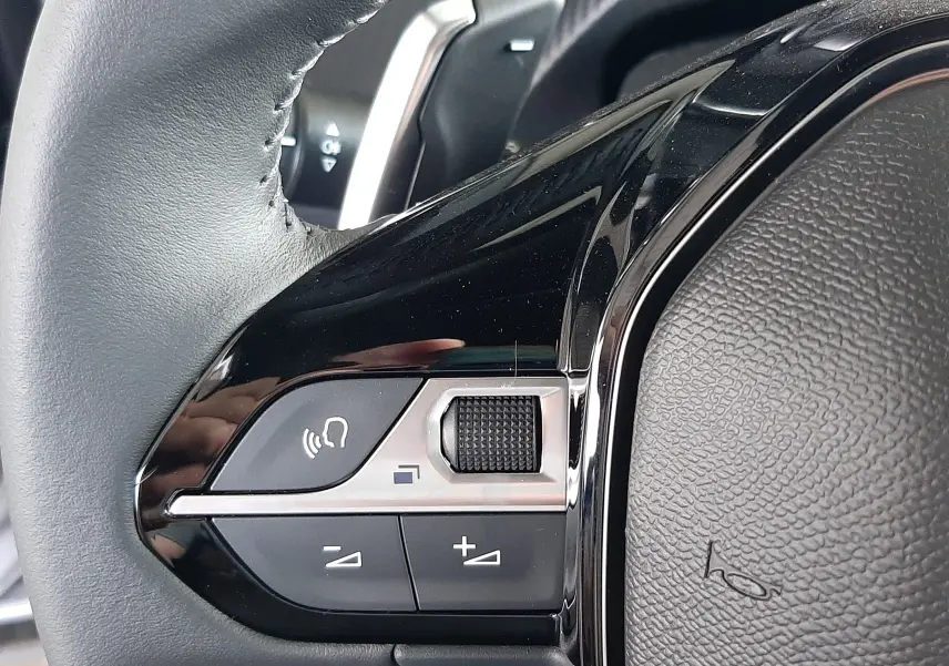 Gros plan sur la commande gauche du volant noir du Peugeot 2008 gris Artense, montrant les boutons de volume et de commande vocale.
