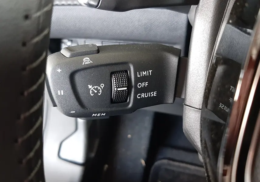 Gros plan sur la commande de régulateur de vitesse à gauche du volant dans un Peugeot 2008 gris Artense 2025.
