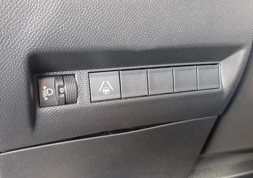 Détail intérieur montrant les commandes de réglage des phares et d'assistance au maintien de voie sur Peugeot 2008 gris Artense.