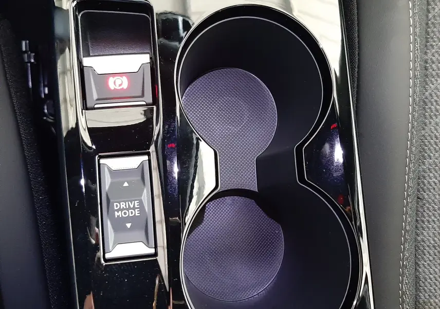 Vue rapprochée de la console centrale noire brillante du Peugeot 2008 1.2 Hybrid avec porte-gobelets et bouton Drive Mode.