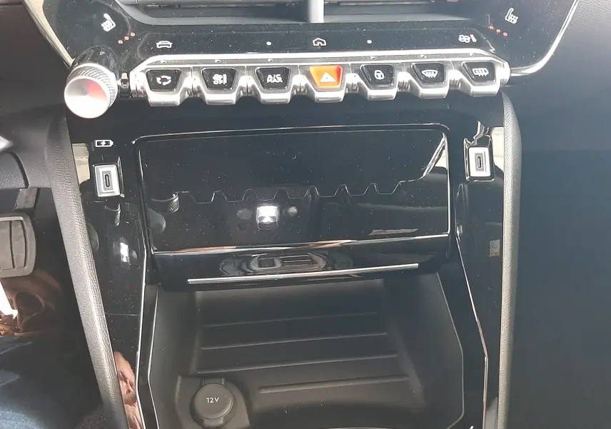 Vue rapprochée de la console centrale noire brillante du Peugeot 2008 1.2 Hybrid 145ch Allure avec commandes tactiles et prise 12V.