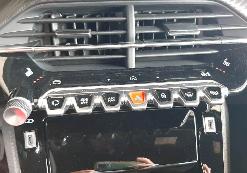Gros plan sur la console centrale noire brillante du Peugeot 2008 1.2 Hybrid 145ch avec boutons de commande et aérateurs.