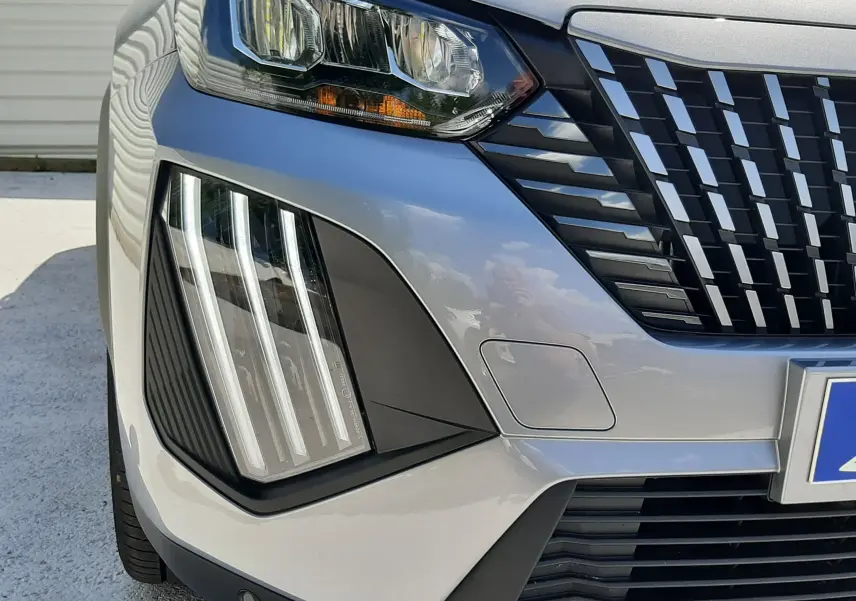 Gros plan sur l'avant droit gris Artense du Peugeot 2008 1.2 Hybrid 145ch Allure avec calandre et feux LED distinctifs.