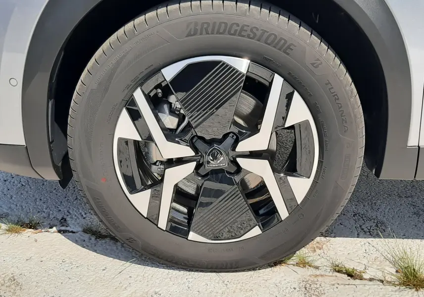 Gros plan sur la roue avant droite d’un Peugeot 2008 gris Artense avec jante alliage noire et argentée.