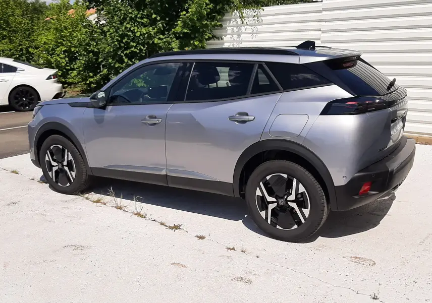 Peugeot 2008 gris Artense vue de profil côté gauche, barres de toit noires et jantes stylisées visibles.