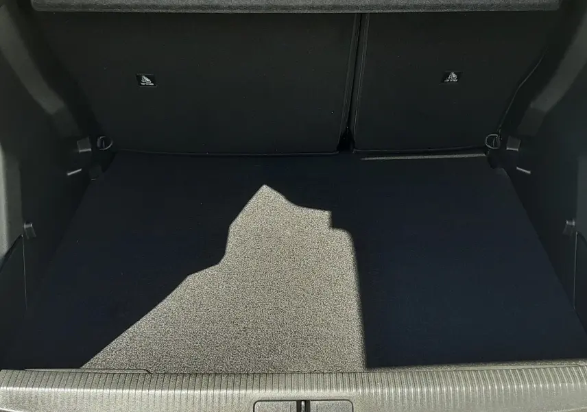 Coffre ouvert vu de l'arrière d'un Peugeot 2008 gris Artense, avec tapis de coffre noir et barres de toit noires visibles.