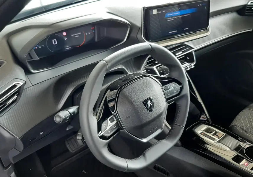 Vue intérieure du poste de conduite du Peugeot 2008 gris Artense 2025, avec volant compact et écran tactile central.