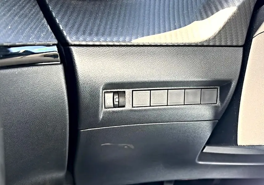 Détail intérieur côté gauche du tableau de bord noir texturé avec commande de réglage des phares du Peugeot 2008 gris 2025.