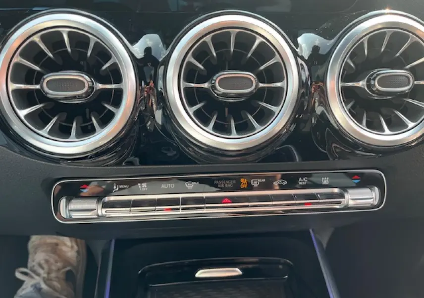 Détail de la sortie d'air ronde chromée et commandes de climatisation dans l'habitacle du Mercedes GLA blanc 2024.