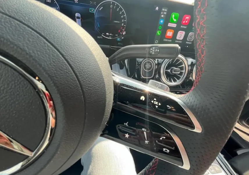 Gros plan sur le volant AMG avec coutures rouges et tableau de bord numérique du Mercedes GLA 250 e blanc 2024 hybride.