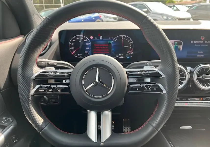 Vue intérieure centrée sur le volant noir perforé avec surpiqûres rouges du Mercedes GLA 250 e hybride 2024.